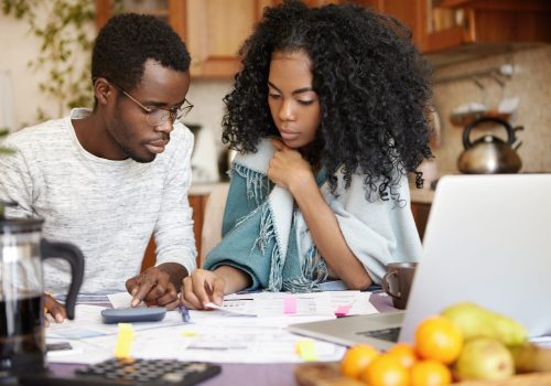 Indoor candid shot of young African-American couple doing paperwork together, calculating domestic expenses and planning family budget, trying to save some money on spending vacations by sea